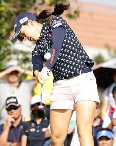 a woman swinging a golf club at a ball while people watch from the sidelines