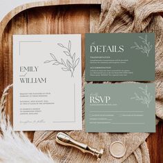 the wedding stationery is laid out on top of a wooden tray with white feathers and greenery