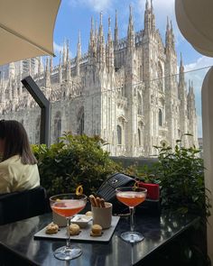 two people sitting at a table with drinks in front of a large castle like building