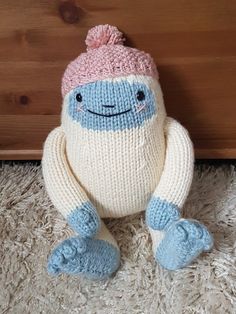 a knitted toy sitting on the floor next to a wooden wall and carpeted area