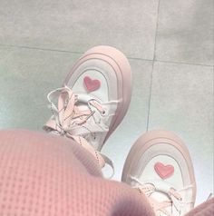 a pair of pink sneakers with hearts on them are seen from the top down, in front of a person's feet