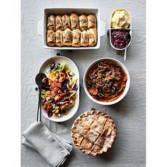 a table topped with plates and bowls filled with food next to pies, bread