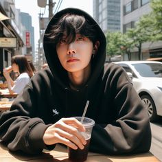 a young man sitting at a table with a drink in his hand and wearing a hoodie