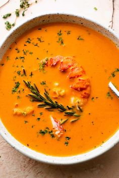 a white bowl filled with carrot soup and garnished with herbs