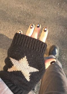 a person's hand with gold and black nail polish holding onto a pair of fingerless gloves