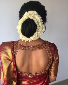 the back of a woman's head with flowers in her hair, wearing a red and gold saree