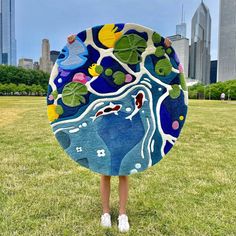 a woman is standing in the grass holding a large piece of art