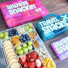 two plastic containers filled with fruit and crackers on top of a wooden table next to some snacks