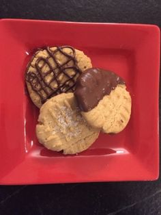 three cookies on a red plate with chocolate drizzled on top and one cookie in the shape of a heart