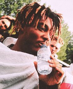 a man with dreadlocks drinking from a water bottle while standing next to other men