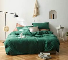 a bed with green sheets and pillows in a white room next to a wooden floor