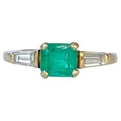 an emerald and diamond ring with two baguets on the side, set in yellow gold