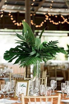 a table set with place settings and greenery in a tall glass vase on the centerpiece