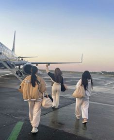 three people walking towards an airplane on the tarmac at sunset or sunrise, with one person in white pants and brown jacket