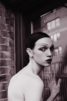 black and white photograph of a naked woman in front of a window with her hand on her face