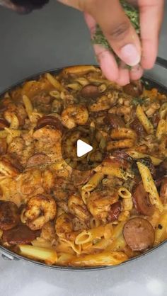 a pan filled with pasta and shrimp on top of a counter next to a person's hand