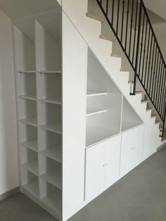 an empty room with white shelves under the stairs and black railings on the second floor