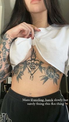 a woman with tattoos on her stomach and chest holding a piece of paper in front of her