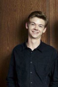 two men standing next to each other in front of a wooden wall and one is wearing a black shirt