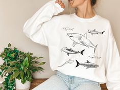 Dive into both comfort and fashion with our captivating illustrated shark sweatshirt! This crewneck is a must-have for shark enthusiasts and anyone seeking a unique addition to their wardrobe. The front of the sweatshirt features an array of beautifully illustrated sharks, bringing the power and beauty of these incredible creatures to life. 🦈🌊 Key Features: 🦈🌊 ✨ Artistic Shark Illustrations: Immerse yourself in the underwater world with our meticulously designed artwork, showcasing a variety of shark species in stunning detail. ✨ Wear Your Passion: Whether you're an avid marine life lover or simply intrigued by the mysteries of the ocean, this sweatshirt lets you express your fascination with these majestic animals. ✨ Cozy and Versatile: Enjoy the perfect blend of comfort and style wit White Crew Neck Top With Shark Design, Shark Species, Shark Illustration, Shark Sweatshirt, Shark Tee, Bday Gifts, Shark Gifts, Shark Lover, Shark Shirt