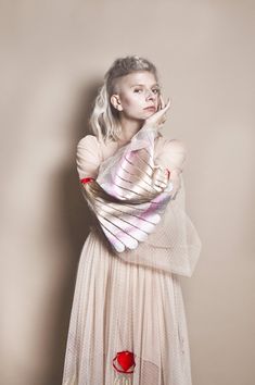 a woman with white hair wearing a dress and holding a bird in her arms while standing against a wall