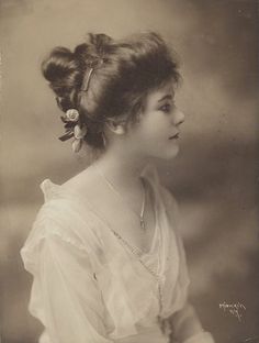 an old photo of a woman with a flower in her hair, wearing a white dress