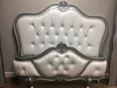 a white bed with silver trim and buttons on the headboard is sitting against a gray wall