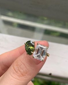 someone is holding two rings with green and white stones on them in front of a window