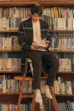 a man sitting on top of a ladder in front of a book shelf filled with books