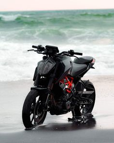 a motorcycle is parked on the beach near the water's edge and waves are in the background