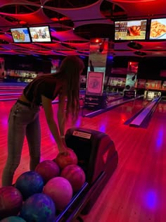 a woman leaning over to pick up some bowling balls