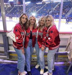 three women in red jackets standing next to each other at an ice rink with fans watching from the stands