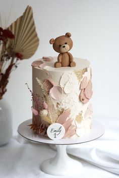 a teddy bear is sitting on top of a decorated cake with leaves and flowers in the foreground