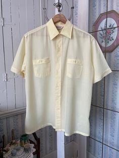 This is a very light weight, semi sheer dress shirt from Kingsport, made from 100 per cent polyester in pale buttery yellow (it's a bit darker than in the photos). The shirt has the original buttons on the front and two chest pockets with matching buttons. Marked size large. The measurements, taken with the shirt lying flat, are: shoulder to shoulder, 19 inches; armpit to armpit, 23 inches; sleeves, 10 1/2 inches; length, 31 inches; bottom edge, 26 inches. In very good condition. Light Yellow Button Up Shirt, Collared Cream Shirt For Summer, Cream Collared Shirt For Summer, Summer Cream Collared Shirt, Yellow Fitted Short Sleeve Shirt, Fitted Yellow Short Sleeve Shirt, Cream Short Sleeve Shirt With Button Closure, Cream Short Sleeve Workwear Shirt, Beige Short Sleeve Shirt For Daywear