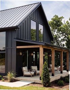 a black house with lots of windows and furniture on the front porch, surrounded by greenery