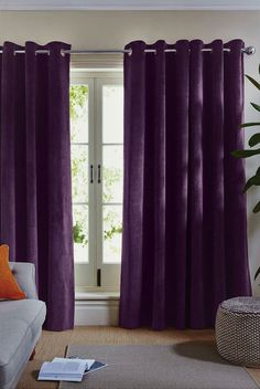 a living room with purple curtains and a gray couch in front of a large window