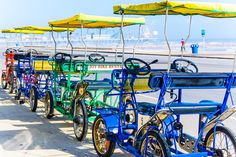 several colorful bicycles are lined up on the side of the road by the beach with yellow umbrellas