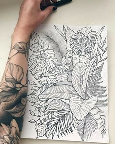 a person holding a pen over a drawing with flowers and leaves on the paper in front of them