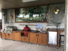 an outdoor kitchen with wood cabinets and grilling equipment on the counter top, under a painting