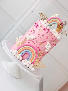 a pink cake decorated with rainbows, clouds and butterflies is on top of a white pedestal