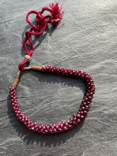 A lovely garnet chip Indian vintage necklace this one is a vintage piece on a lovely traditional extendable cord which works perfectly but has mellowed with age. The stones and bead work are in excellent condition and the colour a warm garnet red rather hard to capture in the photos. It has a maximum length of 40cm. It has a slight fault at the fixing on one side but does not detract from the beauty of this piece.  I am unsure of the age of the piece as it is unsigned but from my minimal researc Traditional Tiny Beads Choker Necklace, Traditional Adjustable Necklaces With Polished Beads, Adjustable Festive Necklace With Round Beads, Festive Adjustable Round Bead Necklace, Festive Adjustable Hand-strung Necklaces, Festive Hand-strung Adjustable Necklace, Handmade Garnet Bead Necklaces, Handmade Garnet Beaded Necklaces, Handmade Garnet Necklaces With Round Beads