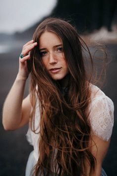 a woman with long brown hair wearing a white dress and holding her hand up to her head