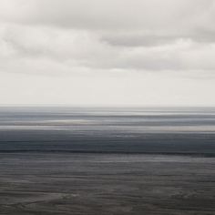 an empty beach with no people on it under a cloudy sky and the ocean in the distance