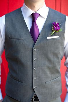 a man wearing a gray vest and purple tie with a flower in his lapel