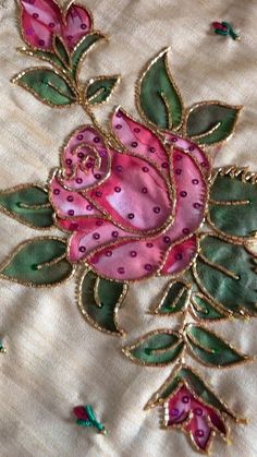 an embroidered rose with green leaves on a white fabric background and gold trimmings