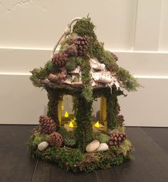 a small house made out of moss with pine cones and rocks on the outside, sitting on a wood floor