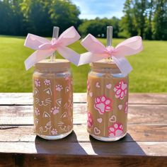 two mason jars with pink bows and hearts on them sitting on a picnic table outside