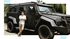 a man standing in front of a black armored vehicle with his arms crossed and looking at the camera