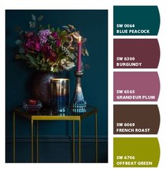 a vase with flowers and candles on a table in front of a wall color chart