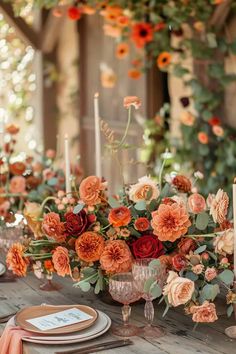 an arrangement of flowers and candles on a wooden table with oranges, pinks and yellows